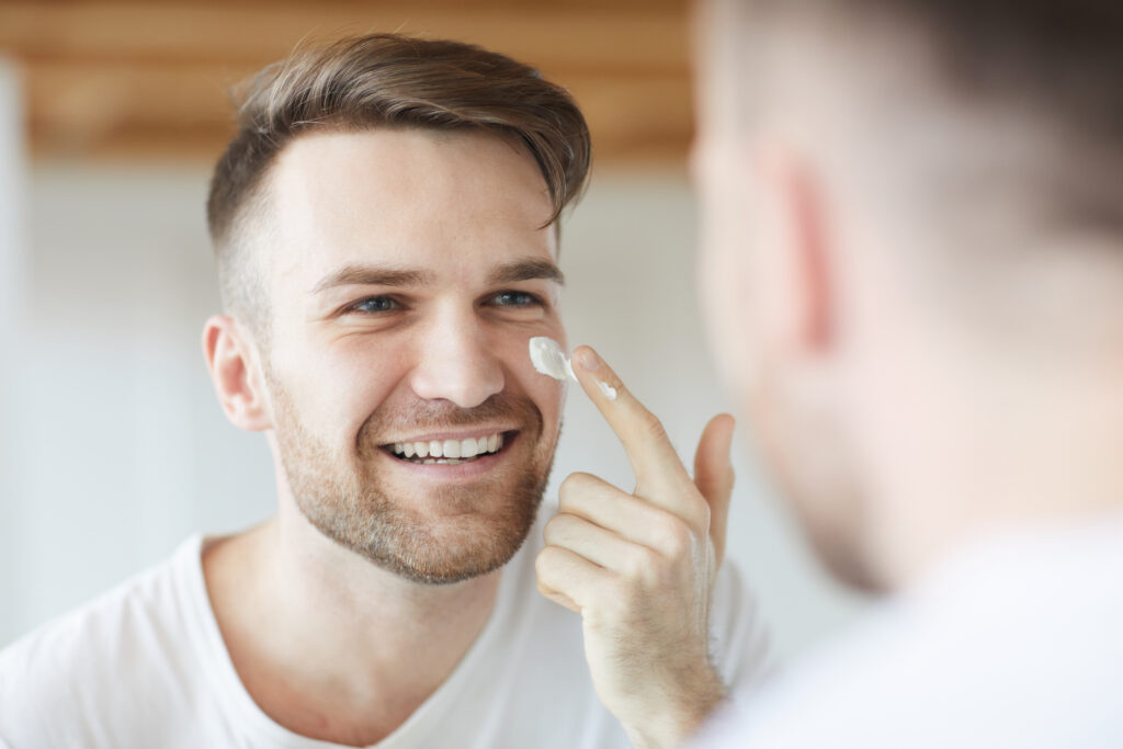 Mann trägt Creme im Gesicht auf und versorgt die Haut mit Feuchtigkeit.
