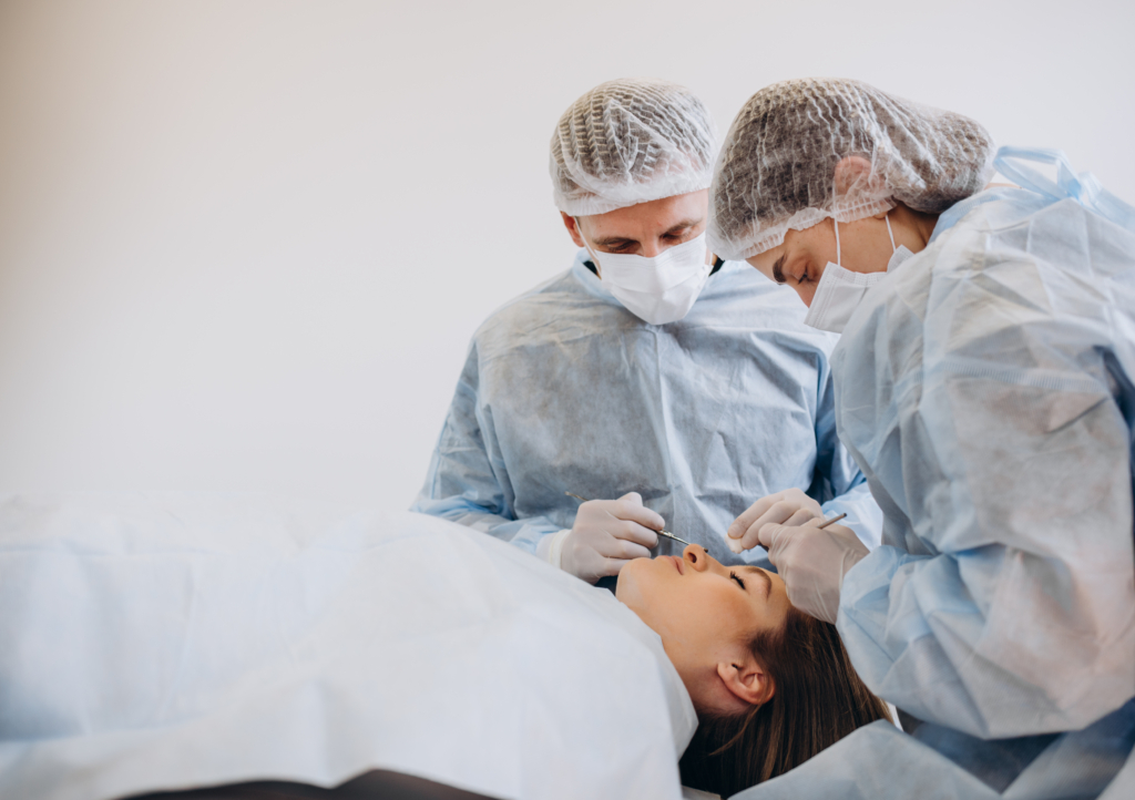 Zwei Chirurgen im Chirurgengewand sehen sich die Nase einer Patientin an