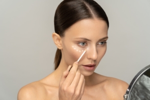 Frau steht vor einem Spiegel und schminkt sich mit einem Concealer