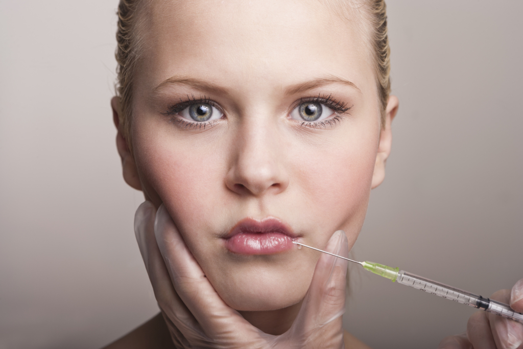 Gesicht eines jungen Mädchens in Nahaufnahme. Eine Hand hält das Gesicht mit weißen Hygiene Handschuhen und spritzt Flüssigkeit in die Lippen