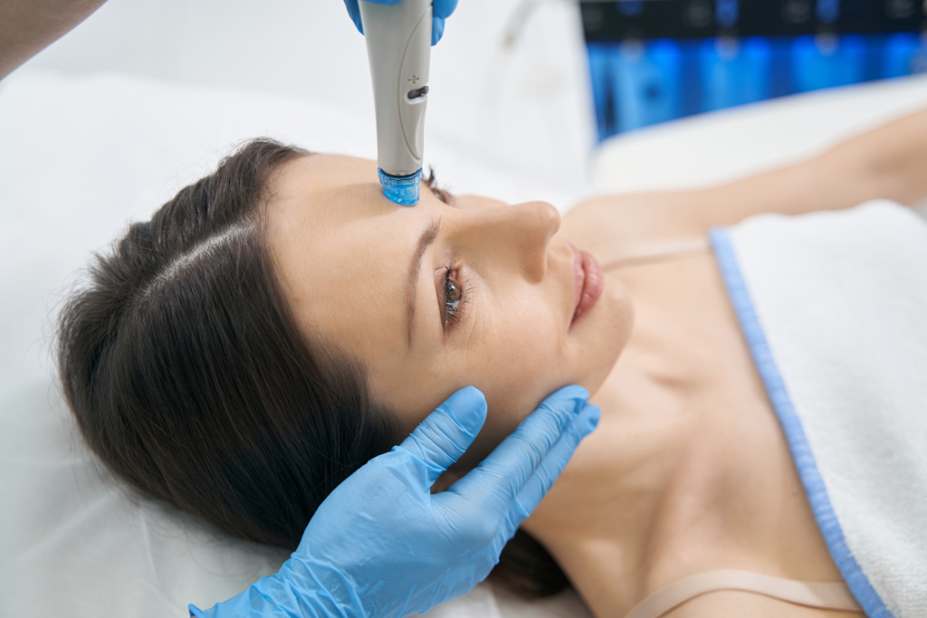 Gesicht einer Frau auf das zwei Hände mit blauen Hygienehandschuhen einen Dermastift setzt