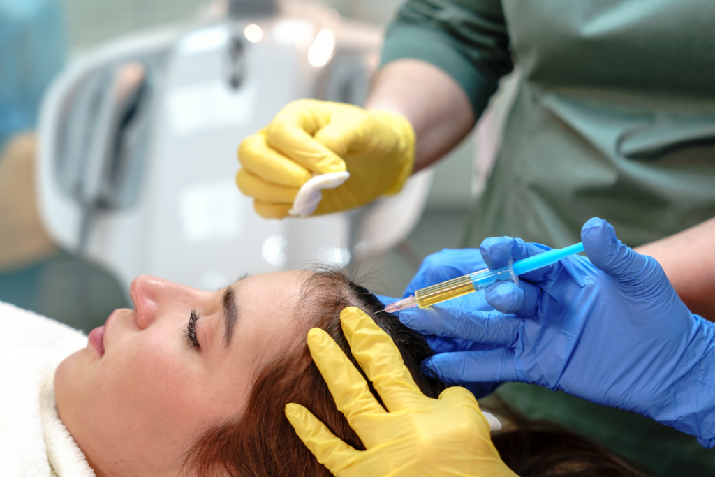 Frau und vier Hände mit gelben und blauen Hygienehandschuhen injizieren ihr mit einer Spritze etwas in die Haare